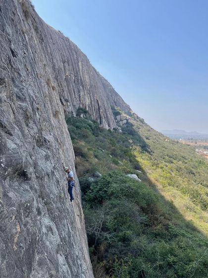 A wide shot showing a climber high up on the massive rock face of Varlakonda. The scale of the cliffs here is truly impressive.