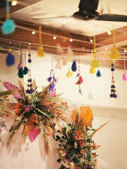 A vibrant and eclectic photo booth backdrop for a Mehendi. We used a mix of pampas grass, colorful dried palms, and hanging tassels to create a fun, textured look.