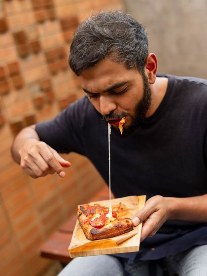 That cheese pull says it all. A slice of our Romana pizza being enjoyed, showing off the gooey mozzarella and airy crust.