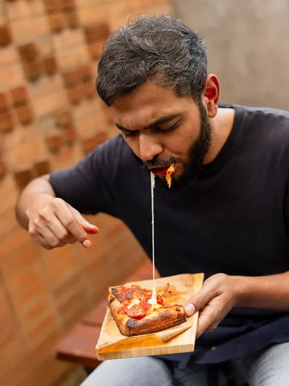 That cheese pull says it all. A slice of our Romana pizza being enjoyed, showing off the gooey mozzarella and airy crust.
