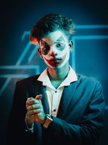 The final look in the Joker series. Here, the focus is on the character's expression and body language, with crossed hands and a direct stare, enhanced by the cool blue and warm orange lighting.
