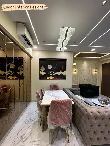 A view of the dining and living area in a Raymond Realty flat, showing the marble-top dining table and the elegant false ceiling with a modern chandelier.
