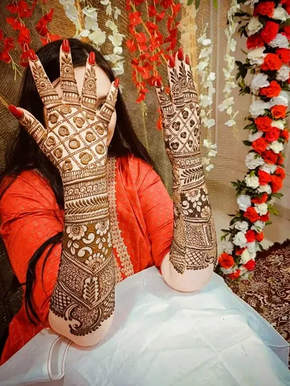 A beautiful shot of a bride displaying her intricate back-hand mehandi against a festive floral backdrop.