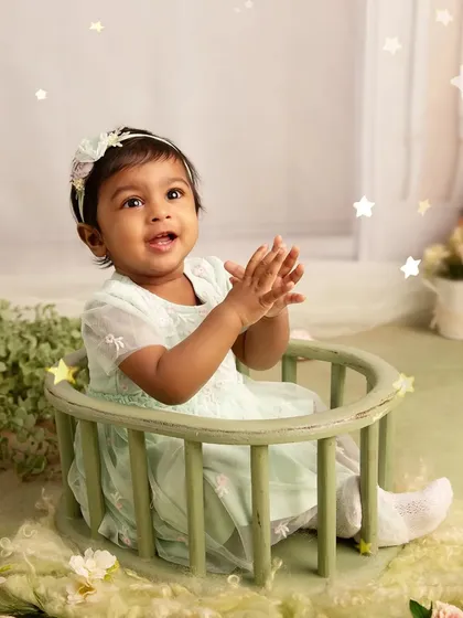 Clapping with joy. This adorable portrait captures a baby's happy expression and playful mood in a soft, mint-green themed studio setup.