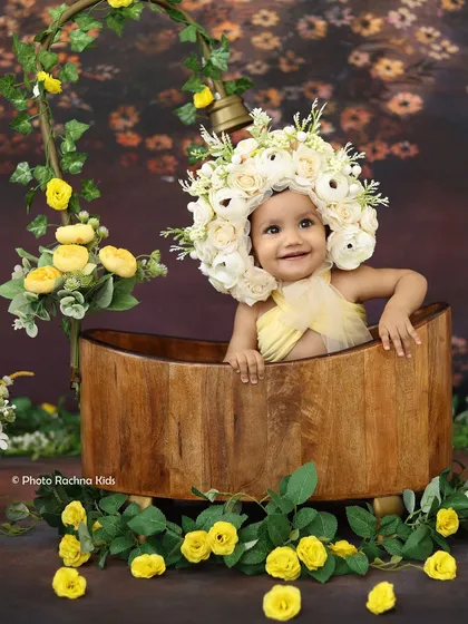 A beautiful toddler girl wearing a floral headpiece smiles from a wooden tub in our yellow flower bath theme.