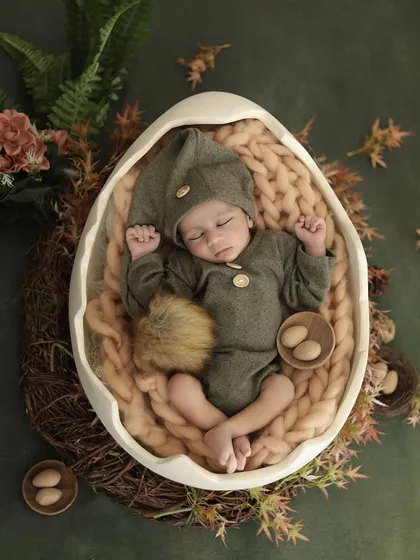 Our unique 'hatching egg' theme for newborns, featuring a baby in an adorable pixie outfit sleeping in a large eggshell prop. This whimsical setup is a client favorite.