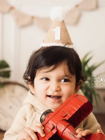 Celebrating one year with a cute party hat and a toy airplane. This close-up captures his cheeky grin and the excitement of his first birthday.