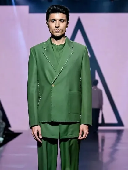 A sharp, tailored look for a male model on the runway. The makeup is completely natural, focusing on shine control and evening out the skin tone for a camera-perfect finish that supports the designer's clean lines.