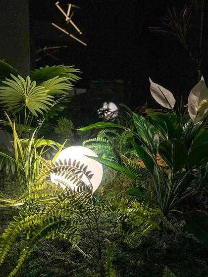 A macro shot of a glowing orb light nestled among faux ferns and peace lily leaves. This highlights our use of lighting to create drama and beauty within our plantscapes.
