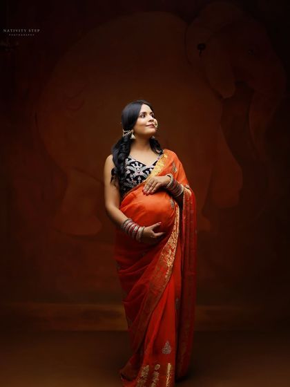 A beautiful three-quarter portrait of an expecting mother in a saree, gently holding her bump. The studio lighting enhances the rich colors of her attire.