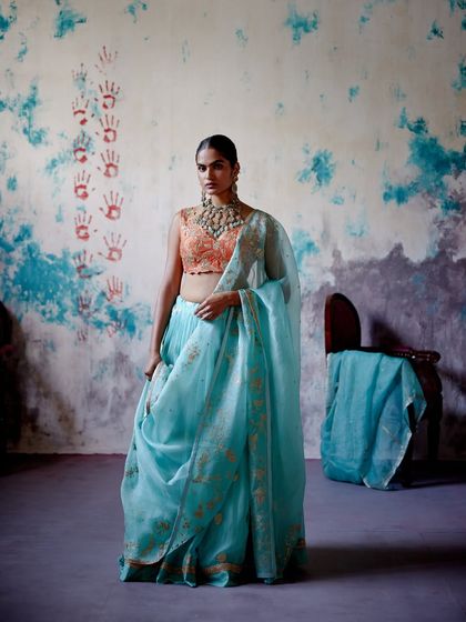 This stunning turquoise saree with a contrasting orange blouse is a celebration of colour. The light, airy fabric and beautiful drape make it perfect for a summer wedding.
