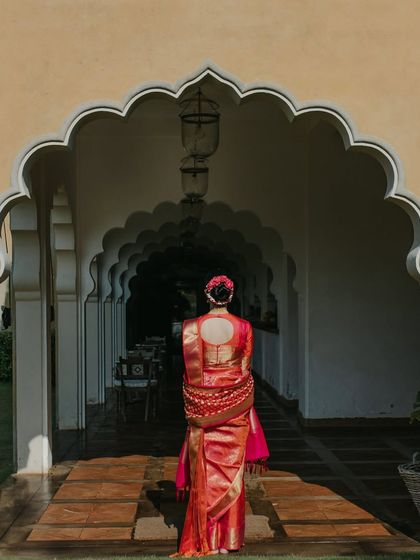 A portrait of the bride from behind, showcasing the stunning details of her red silk sari and floral hair arrangement. The long palace corridor in Sri Lanka adds a sense of grandeur.