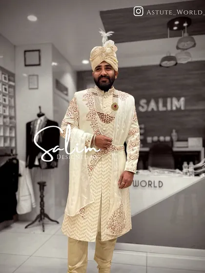 A client trying on his custom wedding sherwani in the studio. This ivory piece features a chevron pattern embroidery with red accents, paired with a matching safa and stole.