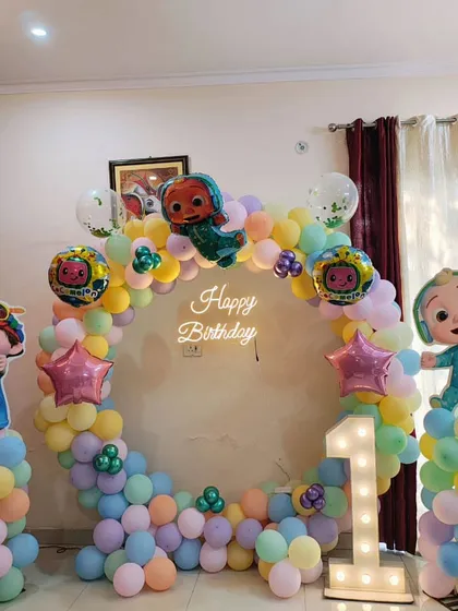 A fun and colourful Cocomelon-themed birthday decoration for a home party, complete with a circular balloon arch and character cutouts.