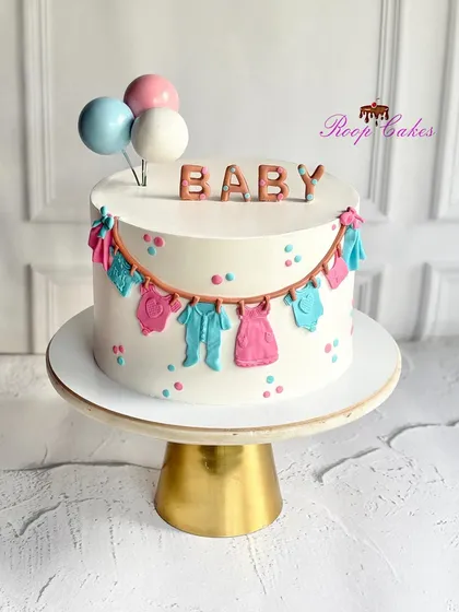 A sweet celebration for the tiniest bundle of joy. This adorable baby shower cake is decorated with a clothesline of fondant baby clothes, pastel polka dots, and balloon toppers.