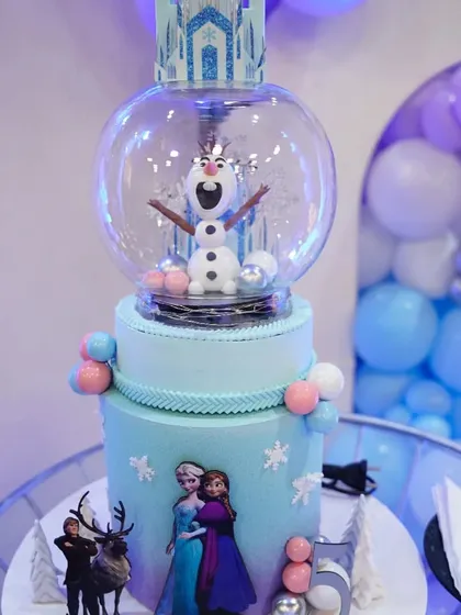An incredible 'Frozen' themed cake featuring a snow globe with Olaf inside. This is a true centerpiece that combines dessert with decoration.