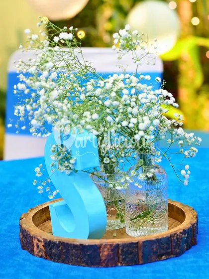 A simple yet beautiful centerpiece featuring baby's breath in glass bottles on a rustic wood slice, personalized with the letter 'S'.