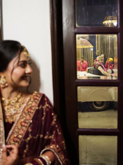 A creative shot of the bride peeking through a window, watching the groom's procession. This photo tells a story and builds anticipation for their meeting.