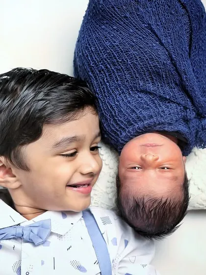 A playful pose with a smiling big brother looking at his newborn sibling from an inverted angle. It's a fun way to add some creativity to a sibling photoshoot.