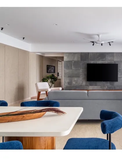 Another perspective of the living and dining space, showing the interplay between the cool tones of the sofa and chairs and the warm wood of the media unit in the background.