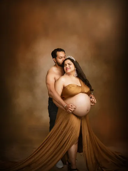 A portrait of golden elegance. The flowing gown and the warm, painterly background create a rich and luxurious feel. Their close embrace and serene expressions make this a truly romantic maternity photo.