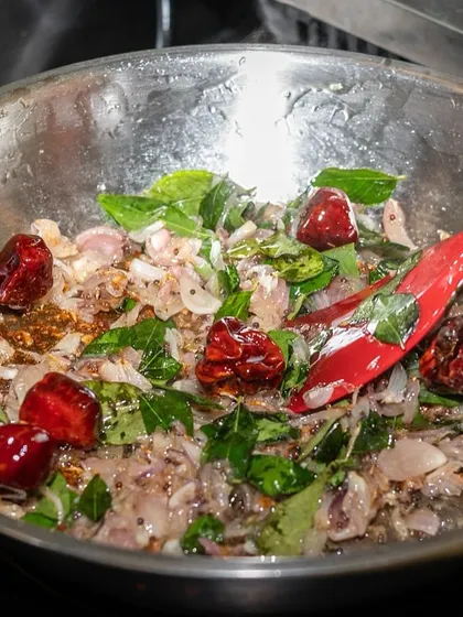 The vibrant colors of spices and herbs sizzling in a pan. This action shot from the Kari Apla kitchen captures the aromatic base of a South Indian dish.