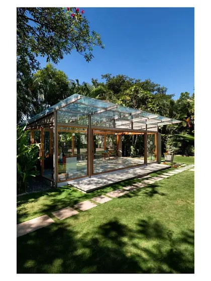 A daytime view of the glass pavilion, where the transparent roof and walls capture the dynamic play of sunlight and shadows from the overhead tree canopy. This space offers an immersive experience of being in the garden while sheltered from the elements.