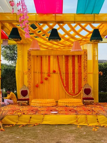 A classic yellow Haldi mandap with traditional seating, decorated with marigold strings and colorful hanging lamps.