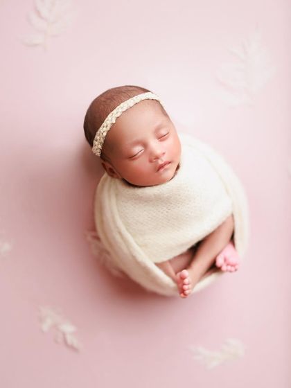 A simple and elegant portrait. The baby is wrapped in a cream-colored knit against a soft pink background, creating a beautiful contrast.