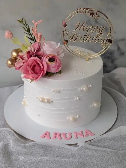 A simple and elegant floral cake for a birthday celebration. The design features a small bouquet of pink flowers and a touch of pearl detailing.