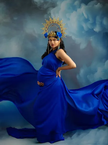 A bold and confident pose. This portrait captures the phenomenal power of a pregnant woman, with the rich blue gown and dramatic sky creating an unforgettable, artistic statement.