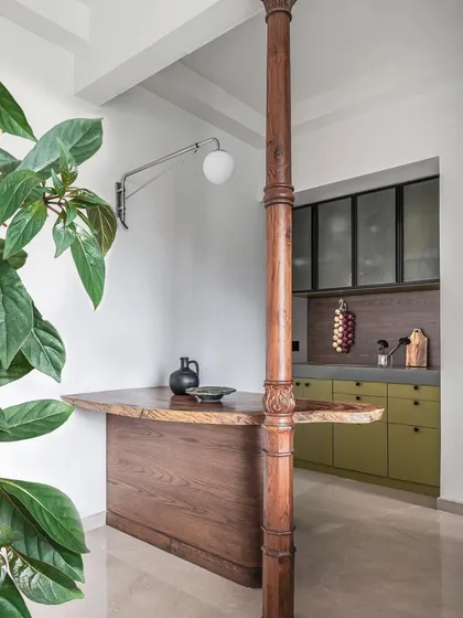 In the compact 'Deux' apartment, we designed a playful and functional bar counter. A live-edge wooden slab is supported by a reclaimed antique column, creating a unique breakfast bar that separates the kitchen from the living area.