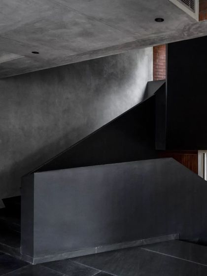 The sculptural black staircase in the Brick House, crafted from pigmented lime plaster, stands as a monolithic element against the polished lime plaster walls and black stone floors.