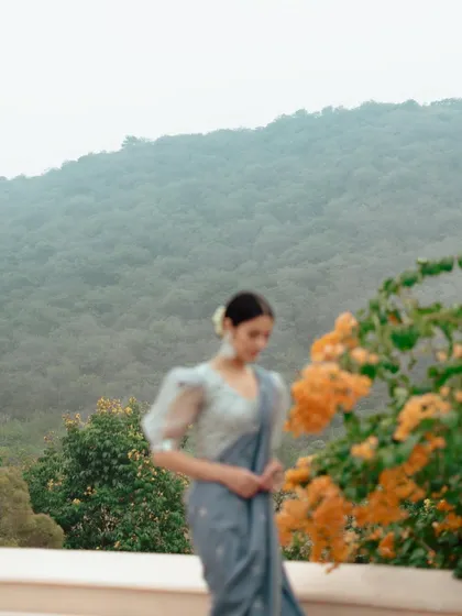 A soft-focus outdoor shot from a lookbook. The model in a saree is set against a hazy mountain backdrop, creating a dreamy and romantic atmosphere.