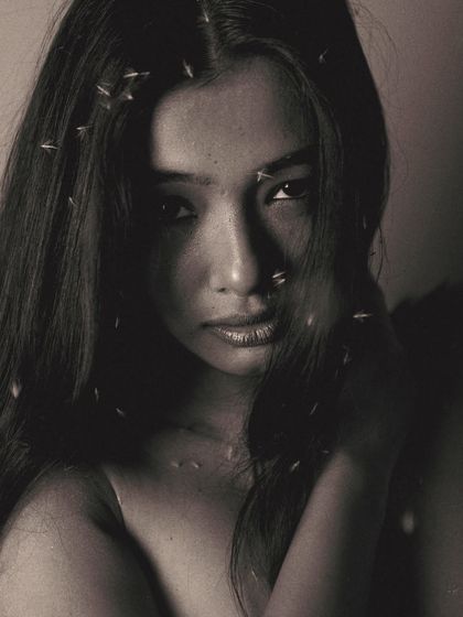 A soft and vulnerable portrait in black and white. The model's expression is gentle, and the specks of light in her hair look like stars, adding to the dreamy, poetic quality of the image.