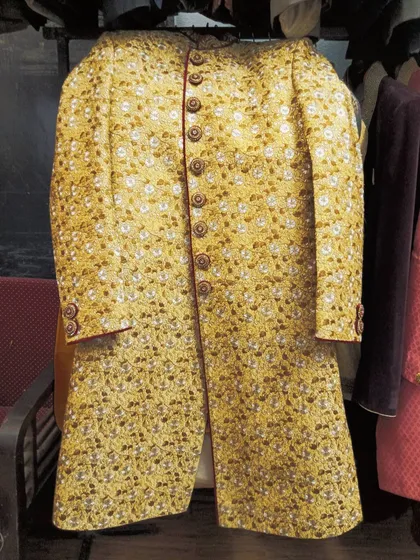 A rich yellow sherwani with dense, intricate embroidery hanging in the store. This is a great option for a Haldi ceremony or for a groom who wants a bright and festive wedding look.
