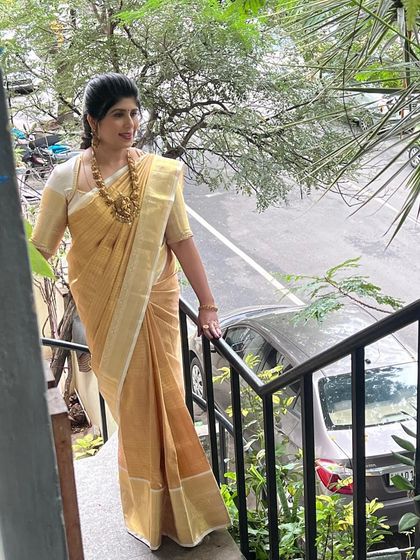 Our client Shilpa in a classic designer gold and off-white silk saree, looking elegant on the stairs.