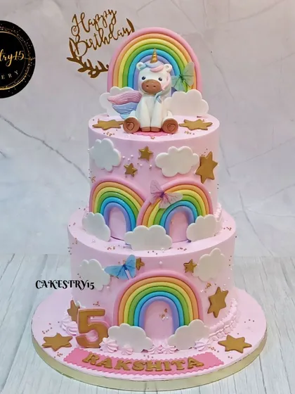 A grand three-tier unicorn and rainbow cake. This pink creation is decorated with multiple fondant rainbows, fluffy clouds, and a unicorn topper for a truly magical 5th birthday.
