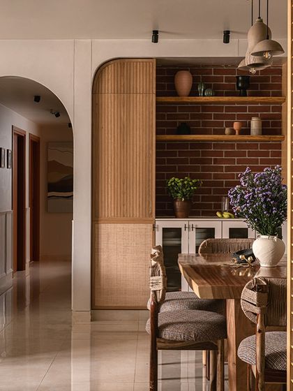 A detail shot of the dining area, highlighting the custom crockery unit with its fluted and cane-detailed doors. The exposed brick niche and live-edge shelves provide a perfect spot for displaying pottery and plants.