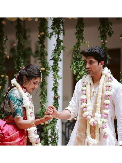 The couple holds hands during their ceremony, with a backdrop of hanging jasmine and rose garlands adding to the romantic atmosphere.