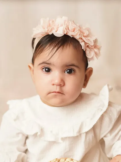 A close-up portrait of the baby girl, her big, expressive eyes looking directly at the camera. Her floral headband completes the sweet, gentle look.