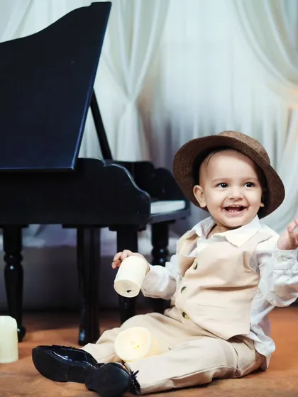 A joyful, laughing toddler in a hat, sitting on the floor with candles during his piano shoot.