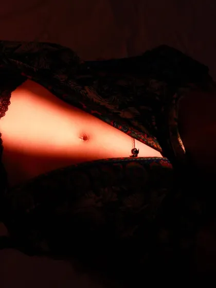 An abstract and moody portrait focusing on a sliver of light hitting the model's midsection, creating a sensual and artistic image.