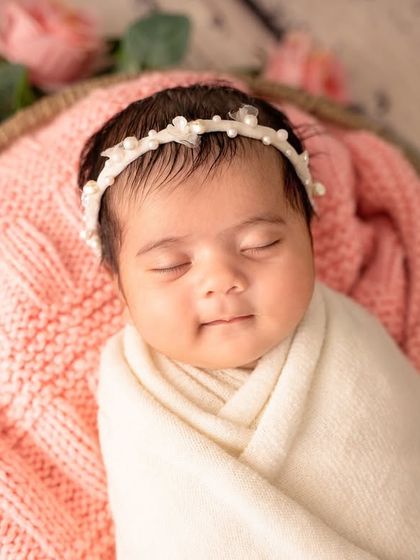 A beautiful, happy smile from a newborn nestled in a basket of soft pink blankets and flowers.