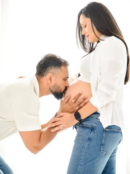 A classic, heartfelt maternity pose. A close-up of the partner kissing the baby bump is a timeless expression of love and excitement for the new arrival. The simple white background keeps the moment pure and focused.