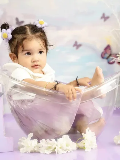 A whimsical first birthday setup with a butterfly and lavender theme. This little girl is sitting pretty in her miniature tub.