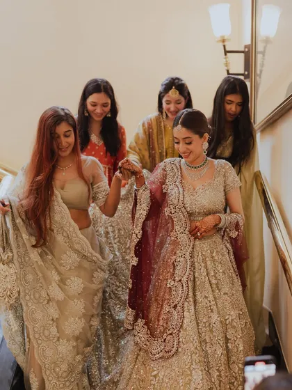 The bride descending the stairs with her bridesmaids, a moment filled with joy. Her radiant makeup ensures she is the center of attention.