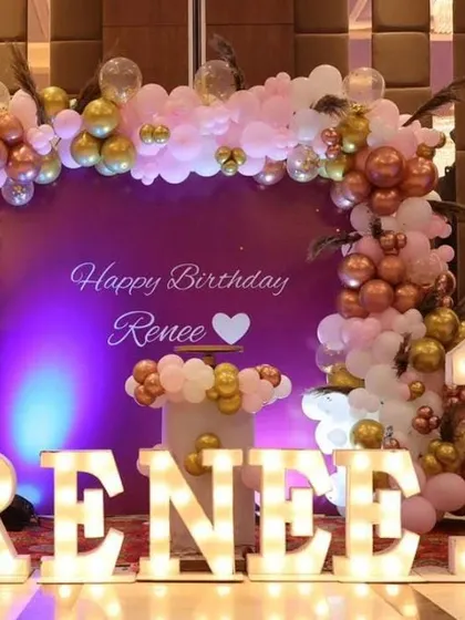 A glamorous first birthday setup for "Renee". This decoration features a purple backdrop with a pink and gold balloon arch, and the baby's name in large, illuminated marquee letters.