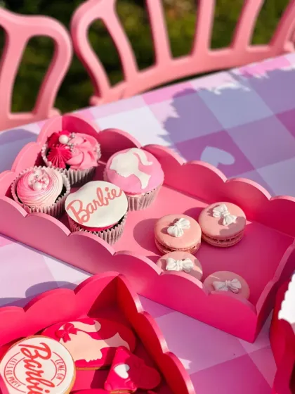 A close-up of the Barbie party desserts, showing custom cupcakes with the Barbie logo and delicate macarons with tiny white bows.