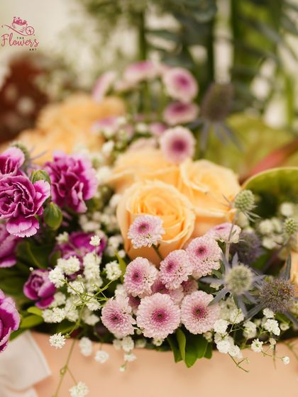 A close-up of the 'Wild Grace' arrangement, highlighting the beautiful combination of peach roses, pink daisies, and purple carnations. The variety of textures and colors makes this a captivating floral gift.
